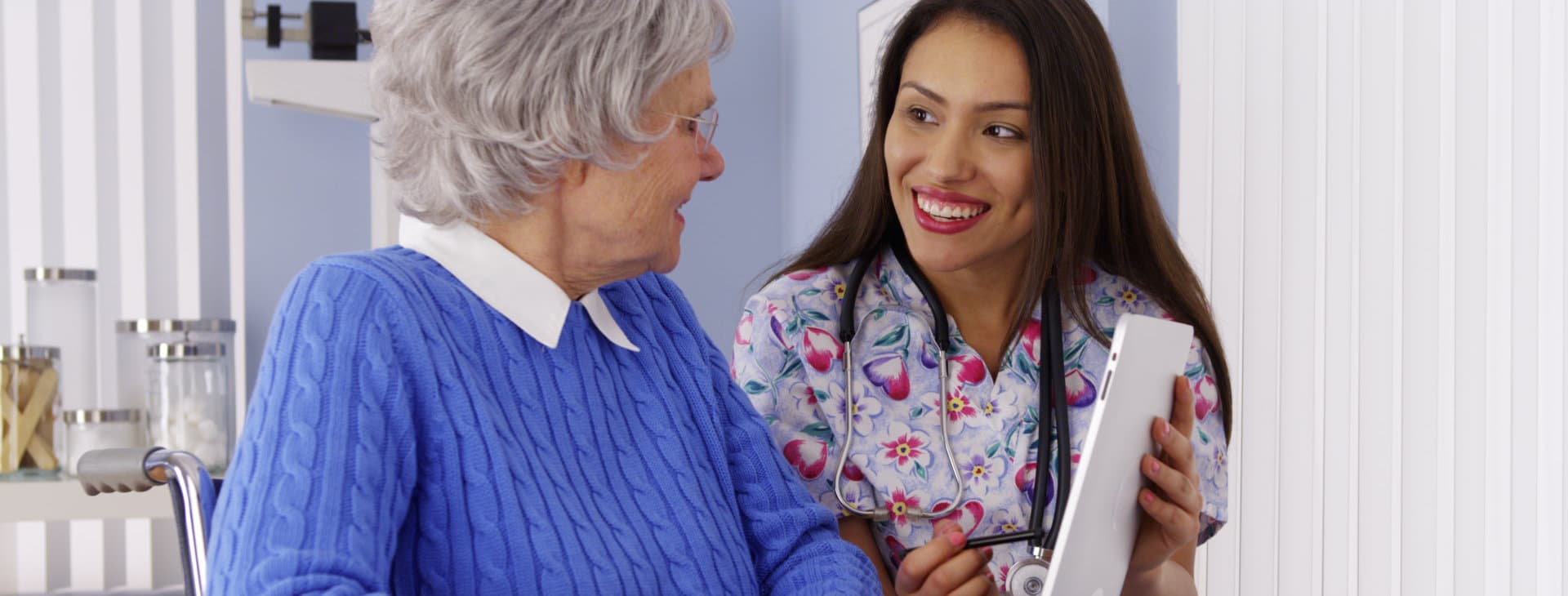 Friendly Mexican caregiver talking to elderly patient with tablet